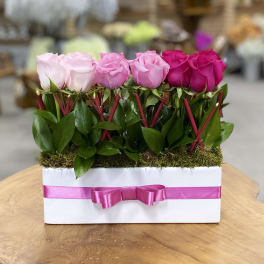 Pink and white roses arranged in a white box with a pink ribbon.