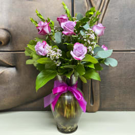 Pink roses arranged in a glass vase with a magenta ribbon