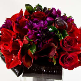 Red roses, purple flowers, and dark calla lilies in a black vase