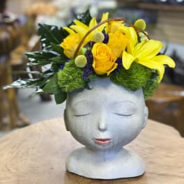 Yellow roses and lilies arranged in a gray sculpted head vase