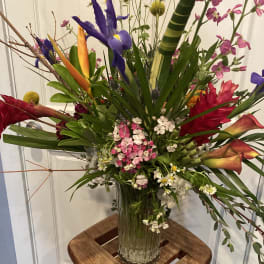 Tropical flower arrangement in a clear glass vase with purple iris and pink blooms