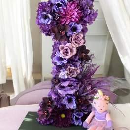 Purple floral number 1 arrangement with a small doll beside it