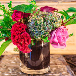 Mixed bouquet in a dark glass vase with pink roses and red blooms