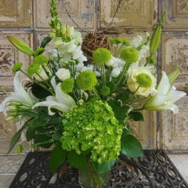 White lilies and green blooms arranged in a glass vase