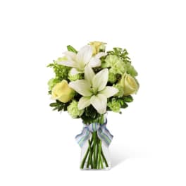 White lilies and pale yellow roses in a clear glass vase with a striped ribbon