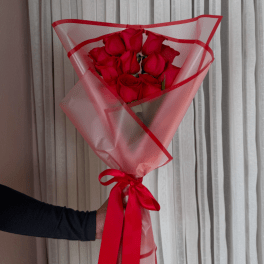 Bouquet of red roses wrapped in pink translucent paper with a red ribbon