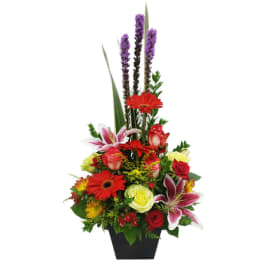 Tall mixed flower arrangement in a black vase with red, pink, yellow, and purple blooms
