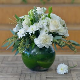 White floral arrangement in a green glass vase with a loose bloom on the table