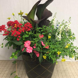 Mixed floral arrangement in a dark decorative pot with red, pink, white, and yellow blooms