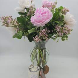 Pink and white flowers in a glass vase with a candle in front