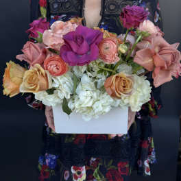 Colorful arrangement of roses and ranunculus with white hydrangeas in a white rectangular box.