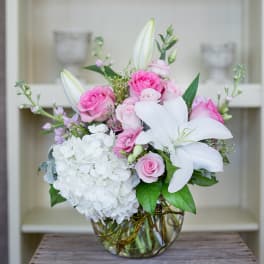Round glass vase with pink roses, white lilies, and white hydrangeas in a compact arrangement