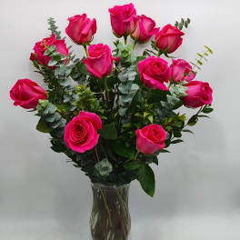 Bright pink roses arranged in a clear glass vase with eucalyptus