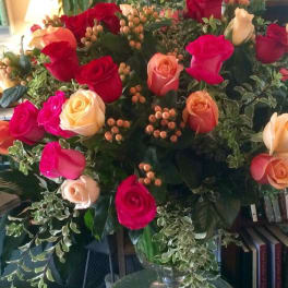 Large bouquet of red, pink, and peach roses with berries in a clear glass pedestal vase