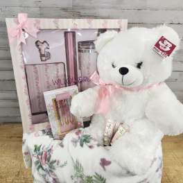 White teddy bear with a pink ribbon beside a floral gift set