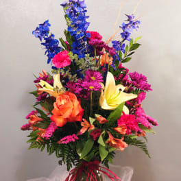 Colorful bouquet with blue delphinium, orange roses, and yellow lilies in a vase