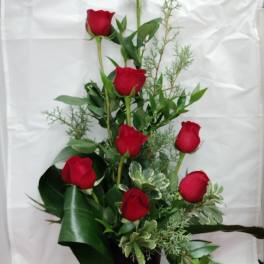 Tall arrangement of red roses in a black vase with greenery