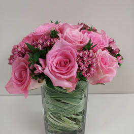Pink roses and small pink filler flowers in a clear square vase