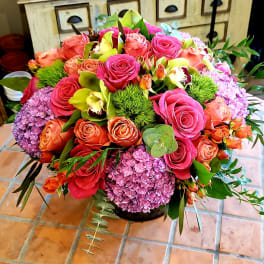 Mixed bouquet of pink and orange roses with purple hydrangeas in a low container