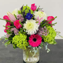 Bright mixed bouquet in a clear glass vase with pink, white, blue, and green blooms