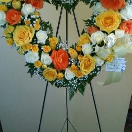 Heart-shaped rose wreath on an easel with yellow, orange, and white blooms