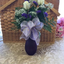 White roses and purple filler flowers in a dark vase with a lavender bow