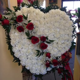 Heart-shaped white floral spray with red roses on a stand