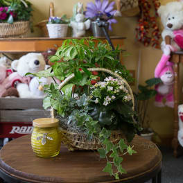 Basket of green plants with small pink flowers beside a yellow candle jar