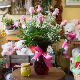 Pink roses in a red glass vase with a pink ribbon