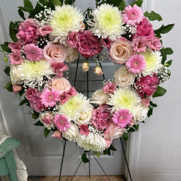 Heart-shaped floral wreath with pink and white flowers on a stand
