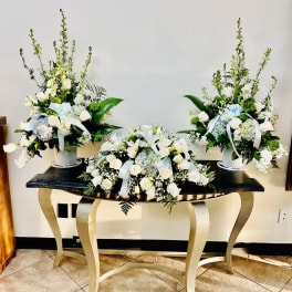 Three white floral arrangements with pale blue ribbons on a table