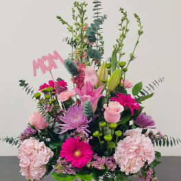 Pink and purple mixed flower arrangement in a white basket with a MOM sign