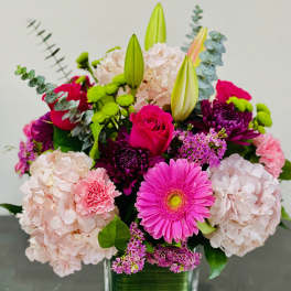 Mixed pink and purple flowers in a square glass vase
