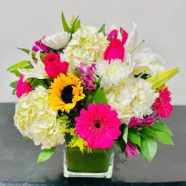 Bright mixed bouquet in a square glass vase with pink, white, and yellow flowers.