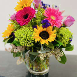 Mixed bouquet with sunflowers, pink gerberas, and roses in a glass vase