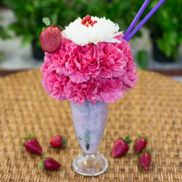 Pink carnations in a tall glass vase topped with a white flower and strawberry garnish
