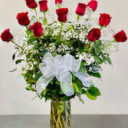 Red roses with white baby's breath in a clear glass vase and white bow