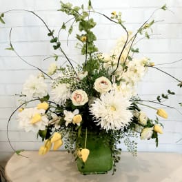 White and pale yellow floral arrangement in a green vase