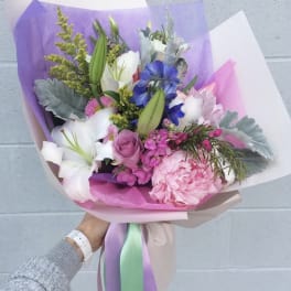 Handheld bouquet of pink, white, and blue flowers wrapped in pastel paper