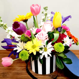 Mixed bouquet in a black-and-white striped box with pink, yellow, purple, and white flowers