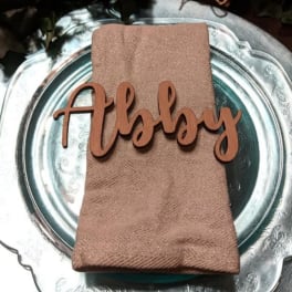 Folded napkin with a wooden "Abby" place card on a silver charger