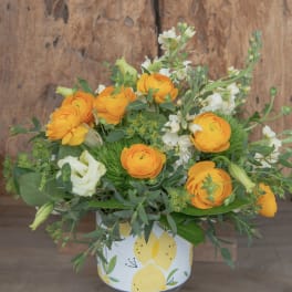 Orange ranunculus and white blooms in a lemon-patterned container