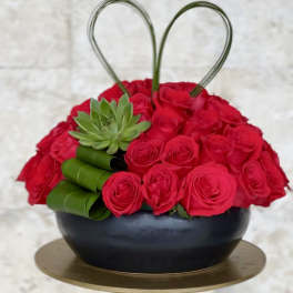 Heart-shaped red rose arrangement in a black bowl with a green succulent accent