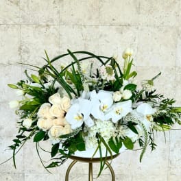 White roses and orchids arranged in a low centerpiece on a stand