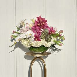 Pink and white floral arrangement in a glass bowl on a gold stand