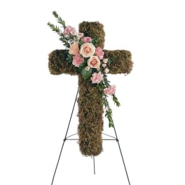 Moss-covered cross with pink roses and carnations on a stand