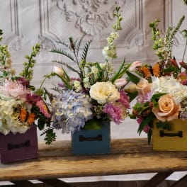Three floral arrangements in colorful wooden boxes with butterfly accents