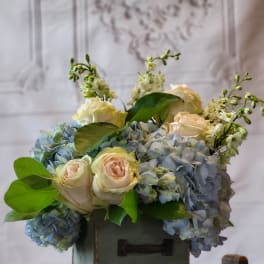 Blue hydrangeas and pale roses arranged in a green box