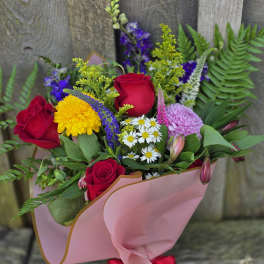 Bouquet of red roses, yellow blooms, and purple flowers wrapped in pink paper