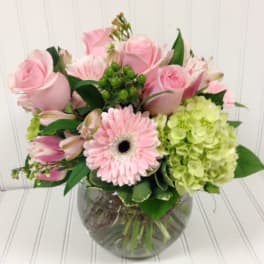 Pink roses and a gerbera daisy in a glass vase with green hydrangea